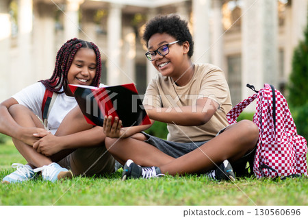 Two teens sitting on the grass and reading something 130560696