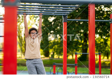 Curly-haired boy doing exercises at the playground in the morning 130560714