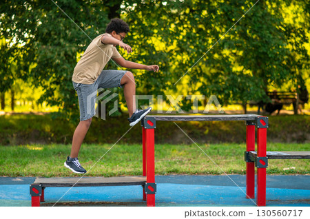 Curly-haired boy doing exercises at the playground in the morning 130560717