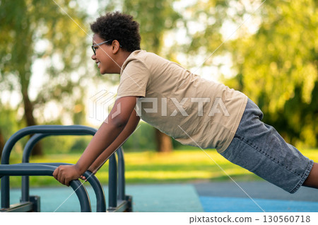 Curly-haired teen exercising at the playground and looking excited 130560718