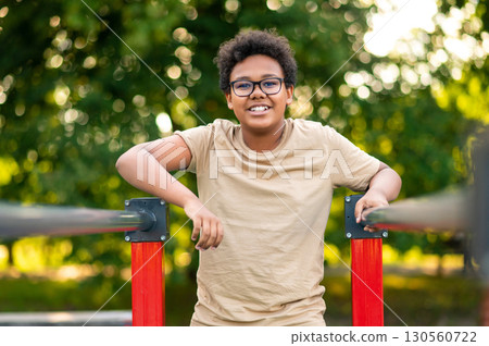 Curly-haired teen exercising at the playground and looking excited 130560722