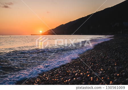 Orange summer sunset in the sea bay with pebble beach and mountains Orange summer sunset in the sea bay with pebble beach and mountains 130561009