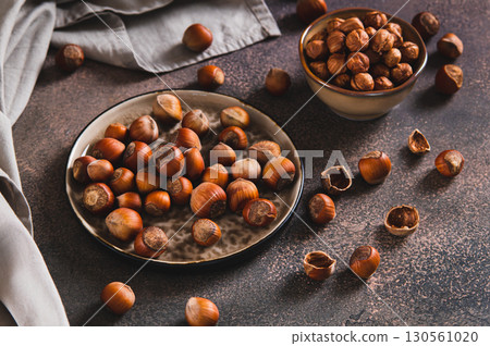 Nutritious unpeeled hazelnuts on a plate and peeled ones in a bowl on a table 130561020