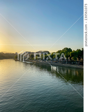 Calm cityscape on the river bank with trees, buildings and calm water under clear blue sky at sunset 130561073