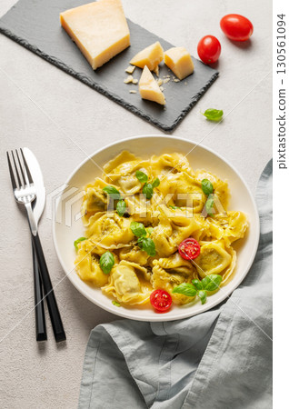 Tortellini pasta with parmesan, pesto and basil in a plate on a light background with tomato Tortellini pasta with parmesan, pesto and basil in a plate on a light background with tomato 130561094