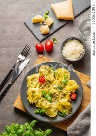 Tortellini pasta with parmesan, pesto and basil in a plate on a wooden board on a dark background 130561098