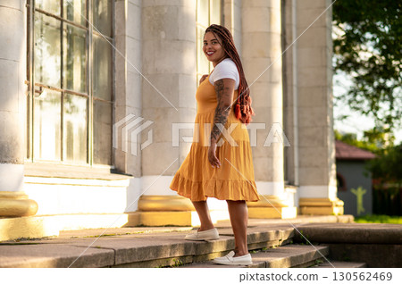 Stylish woman in yellow sundress walking on steps near building 130562469