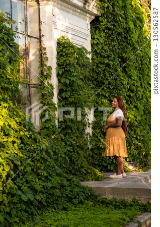 Woman in yellow outfit standing by green leaves during walking Woman in yellow outfit standing by green leaves during walking 130562587