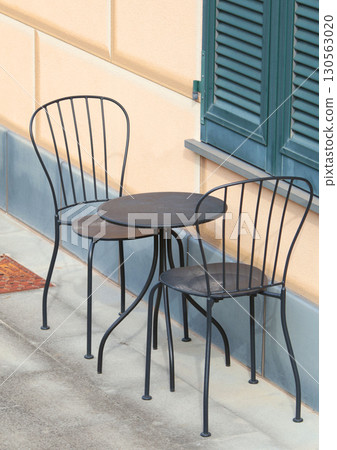 Iron outdoor table and chairs near traditional house, Italy. Garden furniture. Summer yard arrangement. 130563020