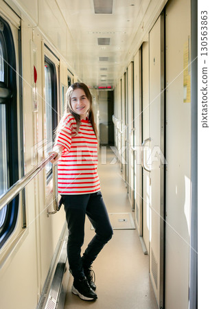 Girl red white striped shirt stands inside sunlit train corridor, expressing joy, confidence, travel 130563863