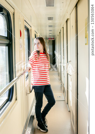 Girl red white striped shirt stands inside sunlit train corridor, expressing joy, confidence, travel 130563864