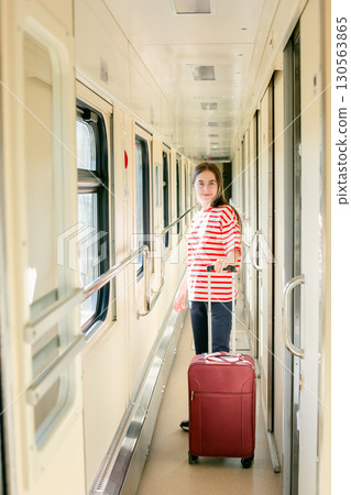 Girl red white striped shirt stands inside sunlit train corridor, expressing joy, confidence, travel 130563865