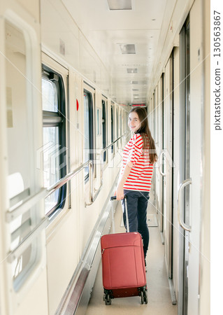 Girl red white striped shirt stands inside sunlit train corridor, expressing joy, confidence, travel 130563867