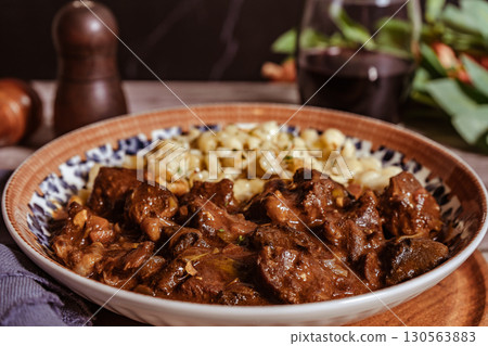 Delicious hungarian goulash with spaetzle and red wine being served on a plate 130563883