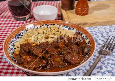 Delicious hungarian goulash with spaetzle and red wine on checkered tablecloth Delicious hungarian goulash with spaetzle and red wine on checkered tablecloth 130563892