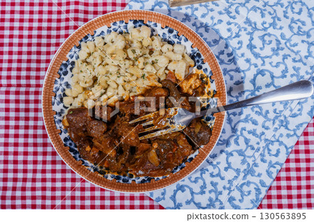 Hungarian goulash with spaetzle on checkered tablecloth: delicious traditional stew 130563895