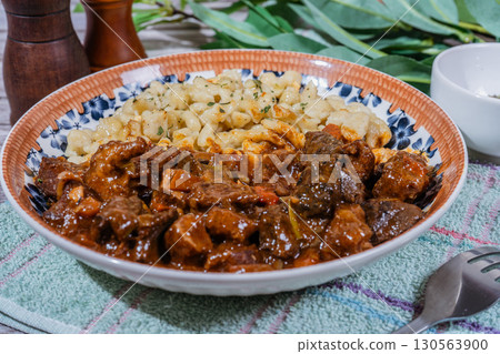 Delicious hungarian goulash with spaetzle, a traditional stew, resting on rustic table 130563900