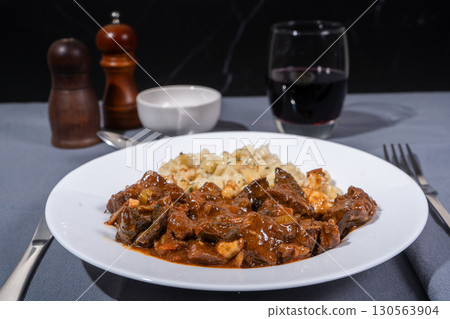 Delicious hungarian goulash with spaetzle and red wine being served on white plate 130563904
