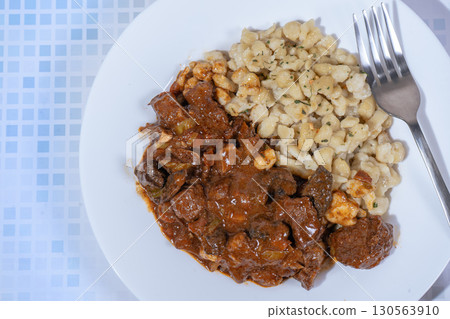 Delicious hungarian goulash with spaetzle garnished with parsley on white plate 130563910