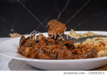 Fork lifting piece of beef from plate of goulash and spaetzle 130563913