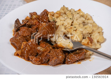 Fork picking up spaetzle from a plate of goulash and spaetzle 130563914