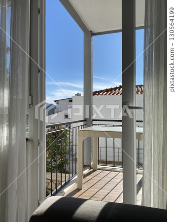 View from airy balcony with wicker table overlooking buildings under clear blue sky 130564199