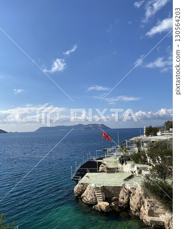 Turkish flag waving on coastline with clear sky and blue sea, capturing tranquil holiday scene 130564203