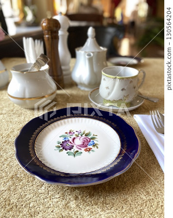 Elegant table setting with floral plate and tea set on luxurious golden fabric background Elegant table setting with floral plate and tea set on luxurious golden fabric background 130564204