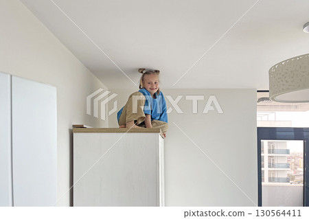 Cute young girl climbing on a high cabinet having fun 130564411