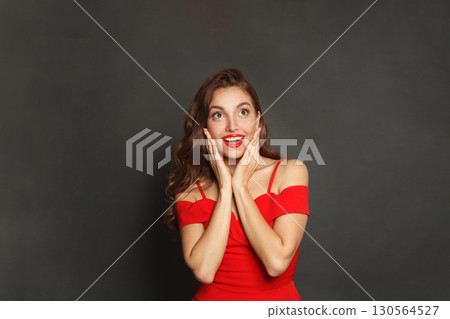 Pretty surprised woman with curly hairstyle and makeup holding her hand with her face  130564527