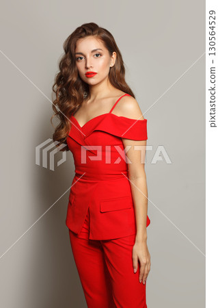 Beautiful young woman in red suit standing against white studio wall background 130564529