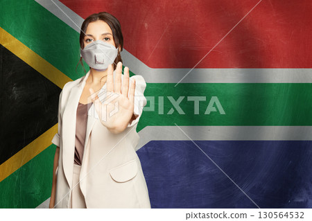 Confident woman in medical mask showing stop gesture open palm hand against flag  130564532
