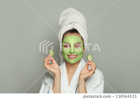Healthy woman in green organic cosmetic face mask holding cucumber slices 130564533