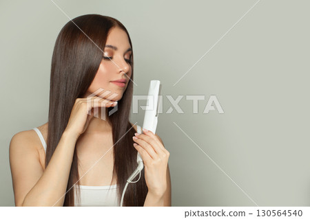 Lovely woman brunette with long straight smooth hairstyle using hair straightener iron  130564540
