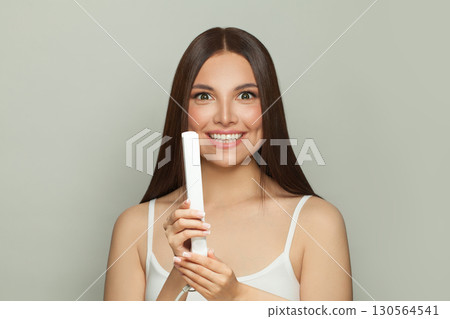 Happy woman brunette with long straight smooth hairstyle using hair straightener iron Happy woman brunette with long straight smooth hairstyle using hair straightener iron 130564541