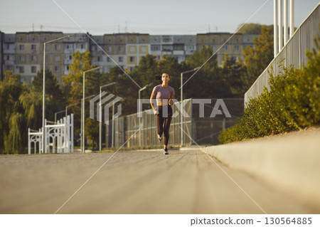 In city streets with green trees and buildings sporty woman running workout health fitness. Motion of running healthy lifestyle self-improvement well-being and energy Woman cardio running workouts. In city streets with green trees and buildings sporty woman running workout health fitness. Motion of running healthy lifestyle self-improvement well-being and energy Woman cardio running workouts. 130564885