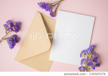 White blank greeting or invitation card with envelope and purple flower decoration on pink background. 130565579