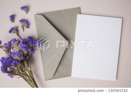 White blank greeting or invitation card with envelope and purple flower decoration on beige background. 130565582