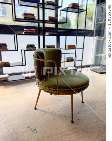 A stylish green velvet chair in a modern interior with books on display. Comfort, design, and contemporary lifestyle. 130565848