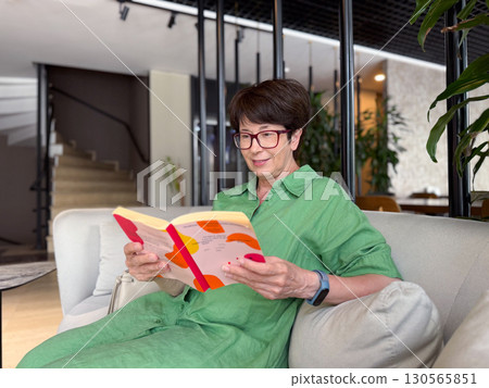 Woman in glasses smiling while holding book. Happiness, reading, and intellectual lifestyle. Woman in glasses smiling while holding book. Happiness, reading, and intellectual lifestyle. 130565851