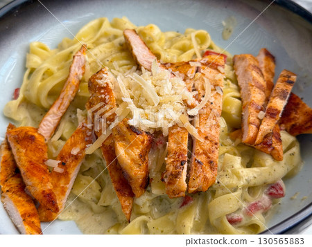 Close-up of pasta with grilled chicken and parmesan in creamy sauce. Gourmet cuisine, indulgence, and food lifestyle in restaurant dining culture. Close-up of pasta with grilled chicken and parmesan in creamy sauce. Gourmet cuisine, indulgence, and food lifestyle in restaurant dining culture. 130565883