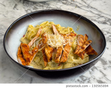 Tagliatelle pasta with grilled chicken and parmesan in creamy sauce. Cuisine, flavor, and gourmet dining in restaurant lifestyle and food culture. Tagliatelle pasta with grilled chicken and parmesan in creamy sauce. Cuisine, flavor, and gourmet dining in restaurant lifestyle and food culture. 130565894
