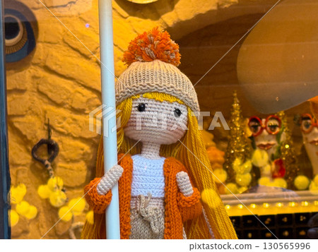 Handmade knitted doll with hat and orange jacket in shop display. Craft, creativity, and childhood memory in cultural tradition and lifestyle. 130565996