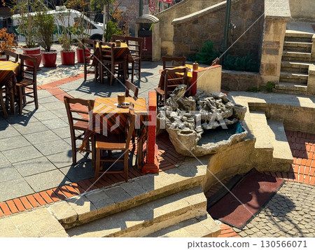 Rustic cafe terrace with wooden chairs and patterned tablecloths. Tradition, leisure, and authentic atmosphere in an old urban courtyard. 130566071