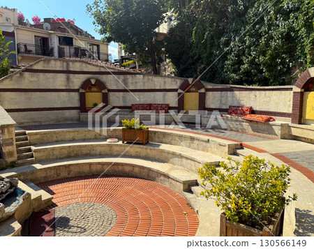 Amphitheater courtyard with stone benches and red patterned cushions. Architecture, heritage, and cultural tradition reflecting outdoor gathering, leisure, and hospitality atmosphere. Amphitheater courtyard with stone benches and red patterned cushions. Architecture, heritage, and cultural tradition reflecting outdoor gathering, leisure, and hospitality atmosphere. 130566149