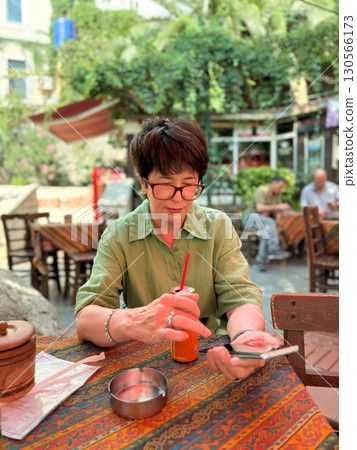 Woman sitting at cafe table drinking soda with straw. Lifestyle, leisure, and hospitality reflecting social interaction, cultural atmosphere, and outdoor relaxation. Woman sitting at cafe table drinking soda with straw. Lifestyle, leisure, and hospitality reflecting social interaction, cultural atmosphere, and outdoor relaxation. 130566173