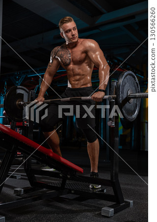 fit man with a strong physique is performing a weightlifting exercise in a gym. Sweat glistens on his skin as he engages in an intense workout surrounded by gym equipment. fit man with a strong physique is performing a weightlifting exercise in a gym. Sweat glistens on his skin as he engages in an intense workout surrounded by gym equipment. 130566260