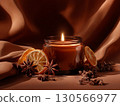 amber glass jar candle burns softly on a backdrop of draped brown fabric 130566977