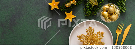 Top view of a Christmas table, featuring an empty plate with cutlery on a green surface. Spruse branches and golden tree decorations set a joyful holiday atmosphere, banner Top view of a Christmas table, featuring an empty plate with cutlery on a green surface. Spruse branches and golden tree decorations set a joyful holiday atmosphere, banner 130568008