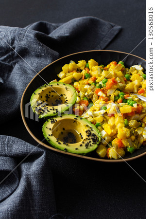 Healthy salad includes boiled egg, tender chicken breast, diced potatoes, vibrant carrots, fresh green peas, and creamy avocado topped with sesame seeds and drizzled with olive oil 130568016